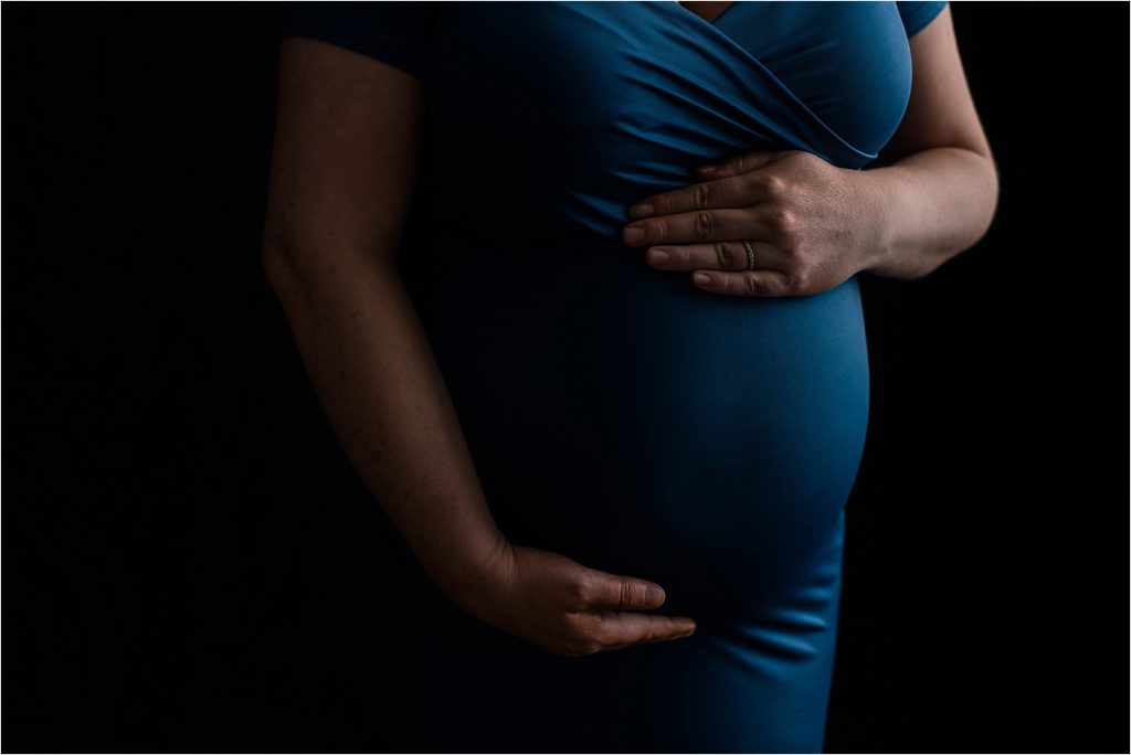 studio maternity session with dramatic lighting on black backdrop with royal blue gown
