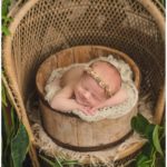 baby girl in farmhouse bucket prop surrounded by plants