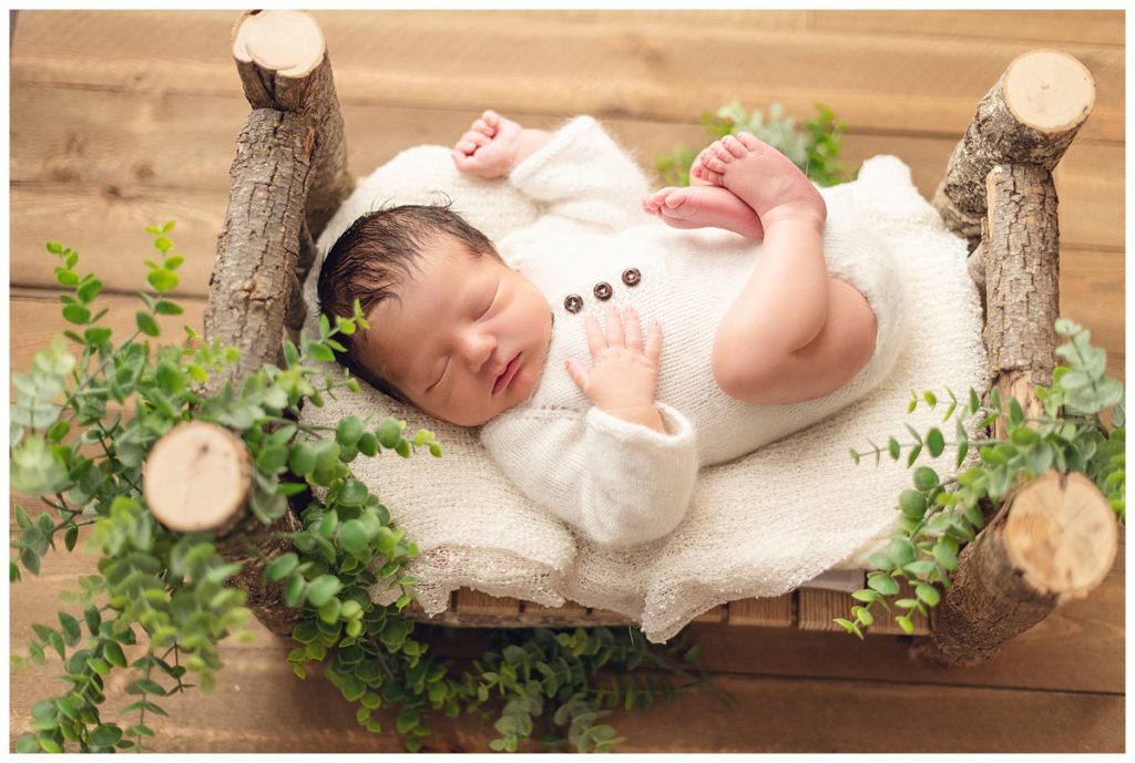baby boy one wood bed surrounded with greenery on handmade wooden log bed