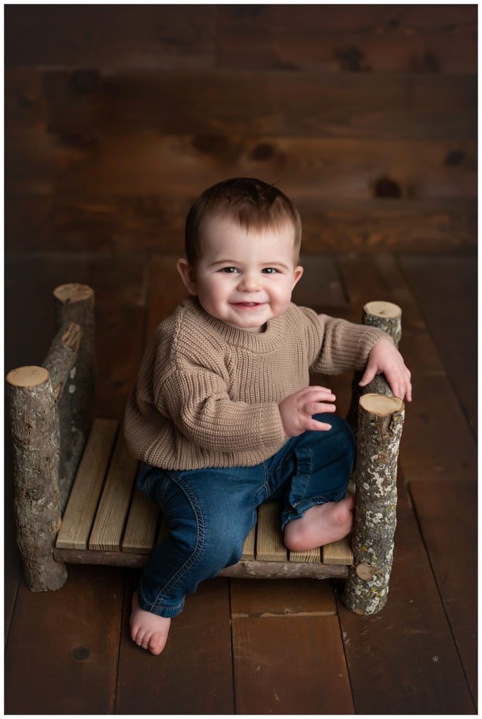baby boy sitting on log bed with one foot up
