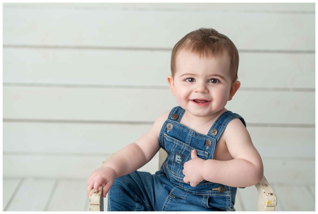 baby boy sitting on chair on white shiplap backdrop