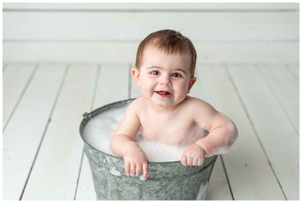 baby boy smiling at camera in basin filled with bubbles