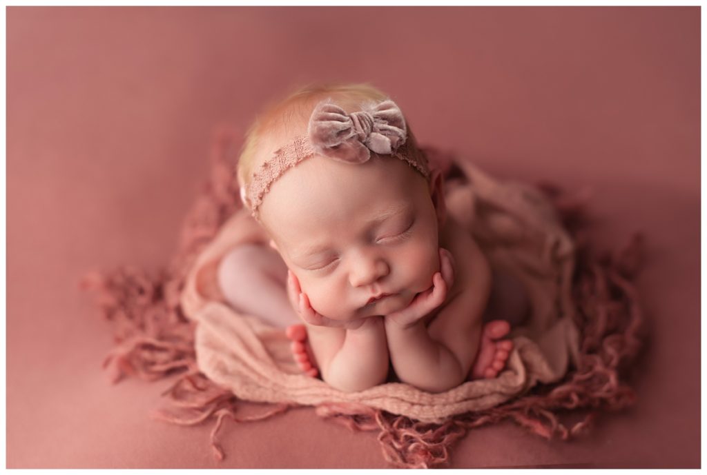 baby girl in froggie pose on rose colored backdrop