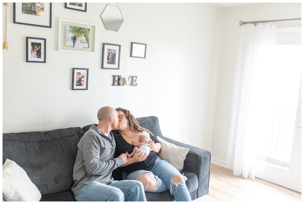 Mom and dad with newborn on couch kissing
