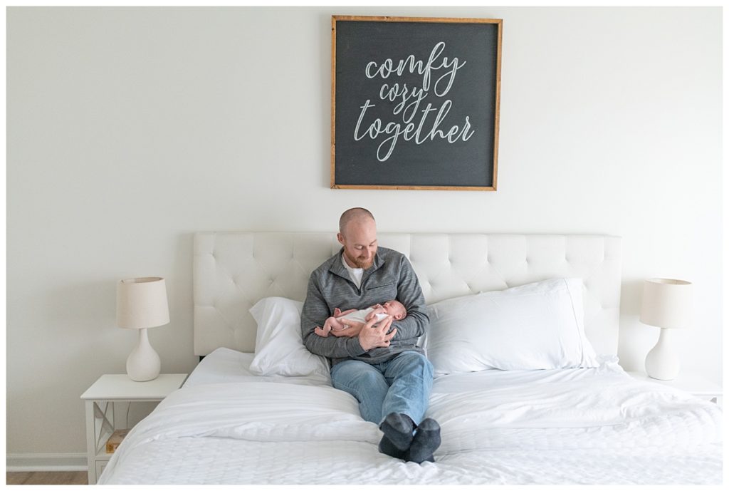 pull back of dad holding baby on bed