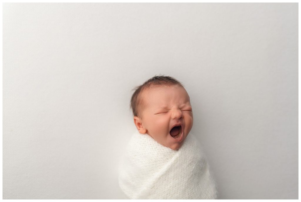 baby boy yawning wrapped in white on white backdrop