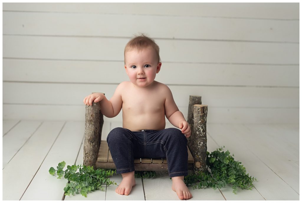 18 month old boy sitting on log bed smiling