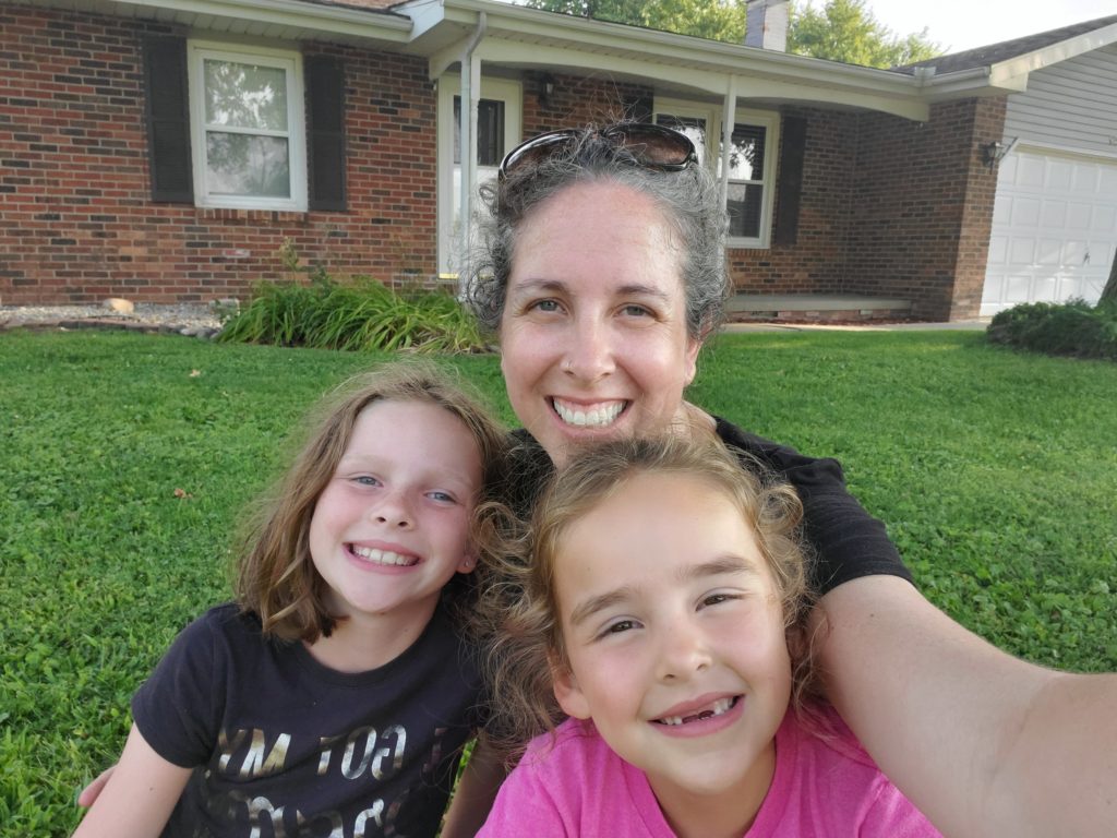 Mom and the girls smiling in front of their old home