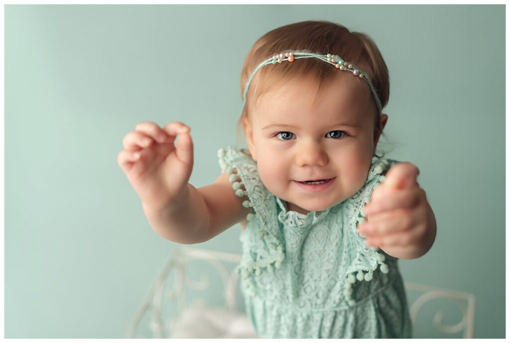 Baby girl on mint green backdrop holding her hands out