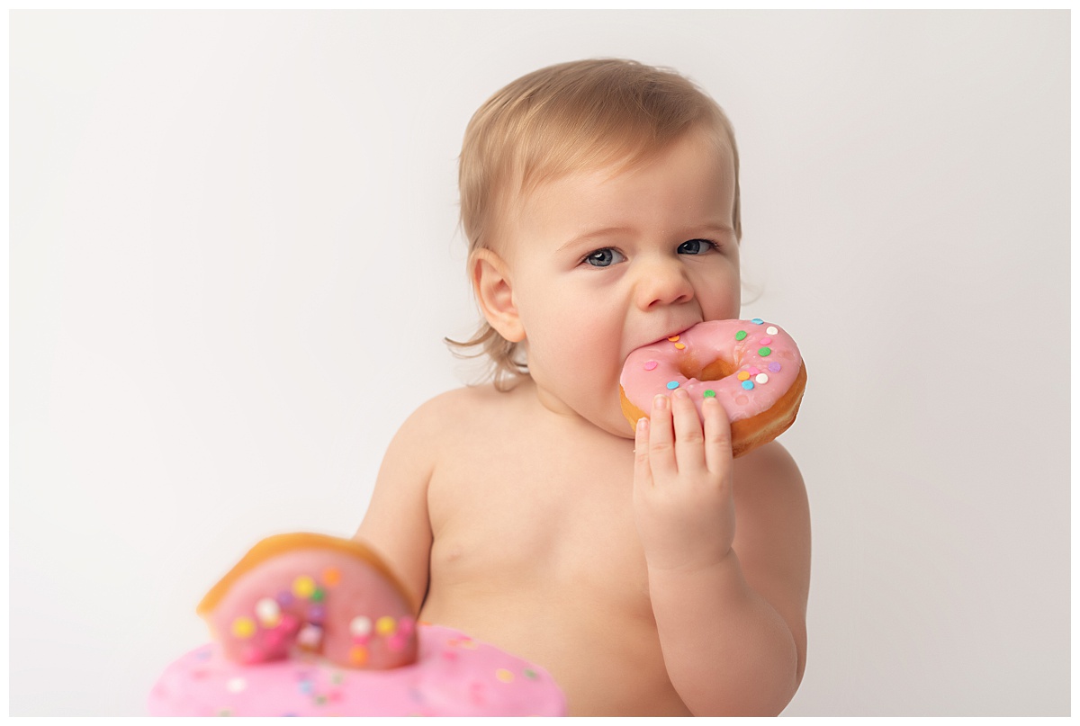 Baby girl eating a pink donut