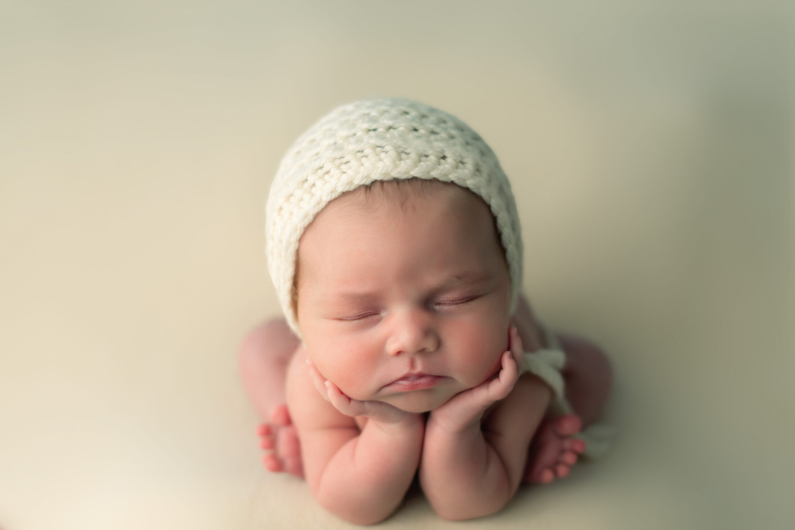 baby girl on white backdrop with white lace bonnet and in froggie pose