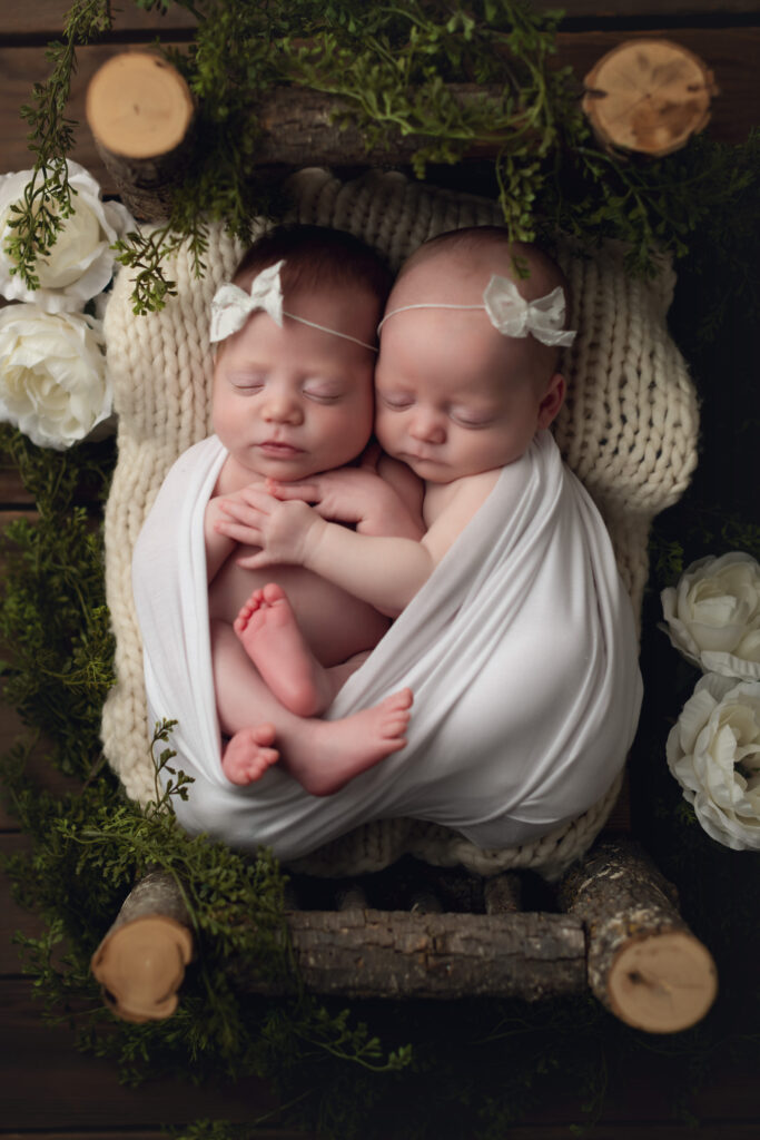 Twin girls on wood bed together surrounded by white flowers and greenery