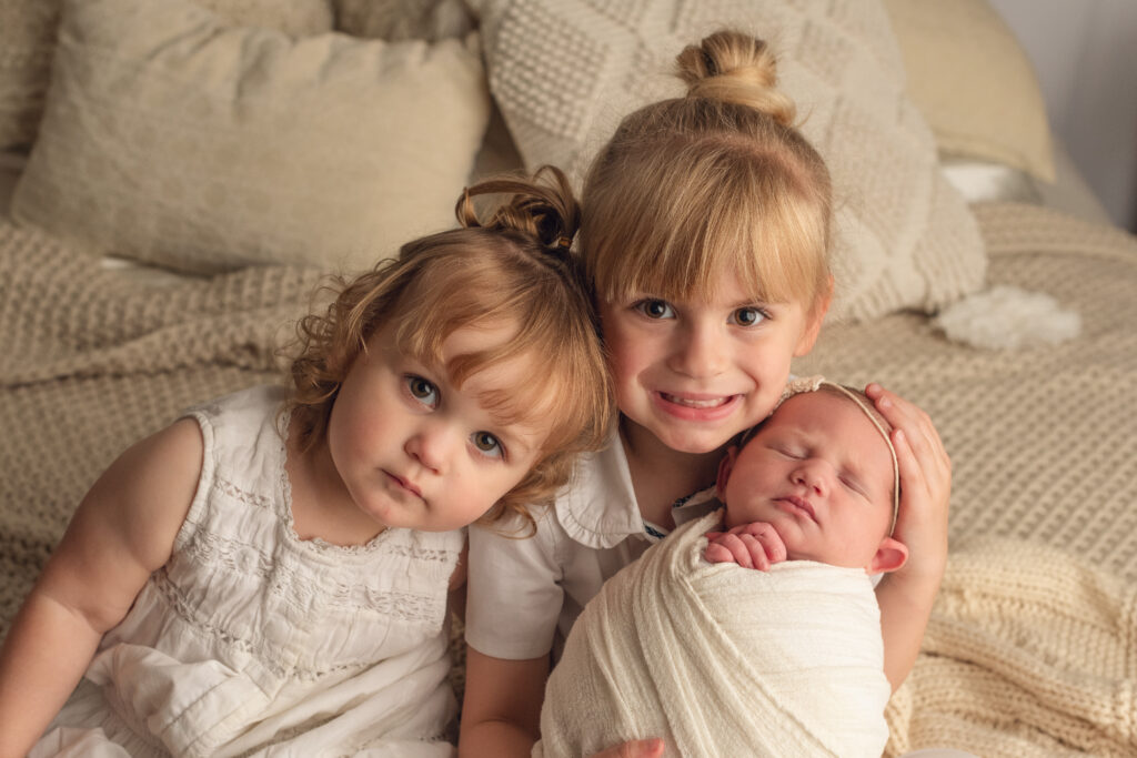 middle sister leaning on oldest sister who is holding baby sister
