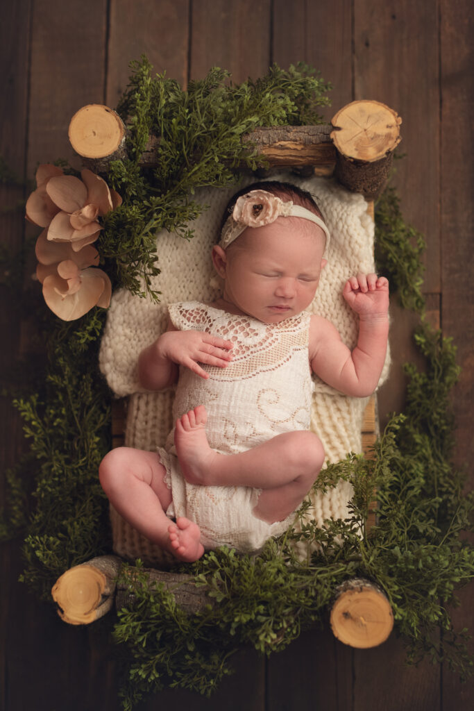 baby girl on log bed surrounded by greenery and florals
