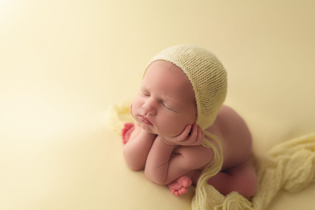baby girl in froggie pose with yellow bonnet one