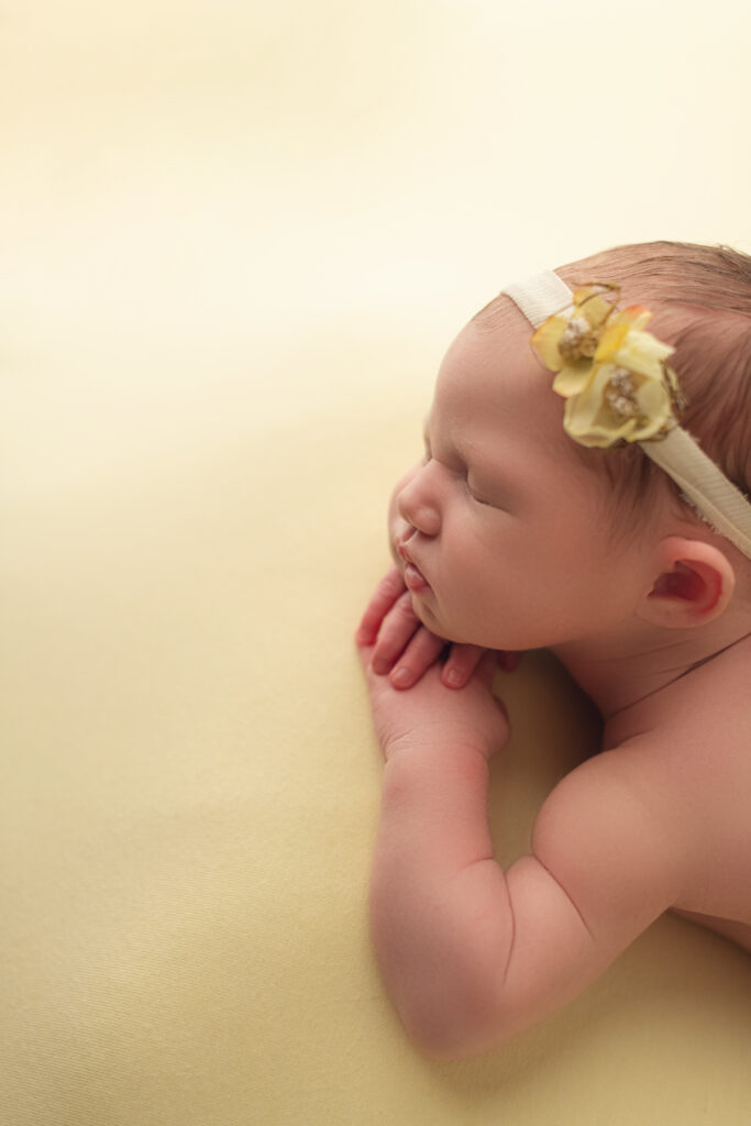 profile view of Newborn baby girl on yellow backdrop with yellow headband