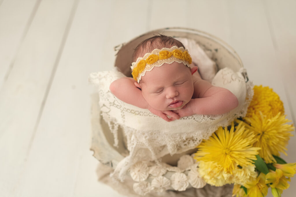 newborn baby girl in white vintage bucket with yellow florals to the side